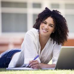 Student lying on grass outdoors studying with notebook